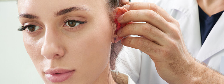 Plastic Surgeon examines a woman's ear.